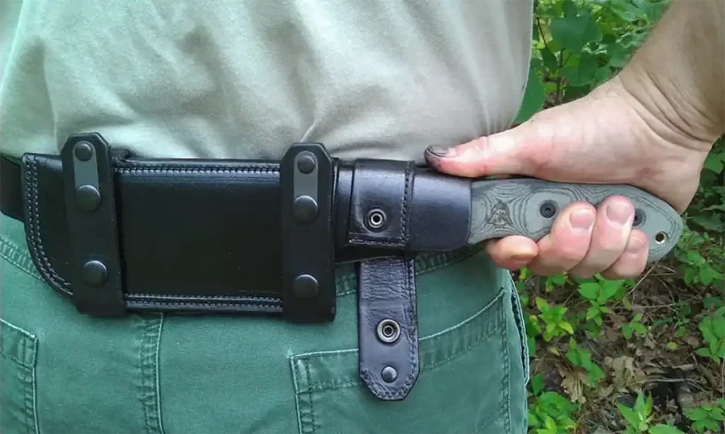 A man's hand drawing the Tops Knives Fieldcraft from it's sheath which is worn in the front horizontal carry position. 